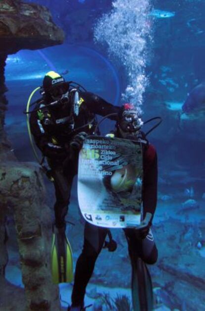 Dos buceadores despliegan el cartel anunciador de la presente edición del Ciclo Internacional de Cine Submarino de San Sebastián en uno de los tanques del Aquárium donostiarra.