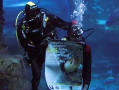 Dos buceadores despliegan el cartel anunciador de la presente edición del Ciclo Internacional de Cine Submarino de San Sebastián en uno de los tanques del Aquárium donostiarra.