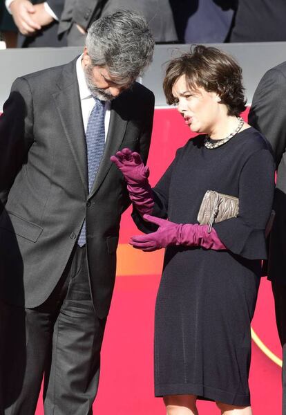 Soraya Sáenz de Santamaria, vestida de negro con guantes morados y bolso cartera de Miu Miu