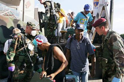 Varios evacuados de New Orleans bajan, cargados con algunas de sus pertenecias, de un caminón militar.