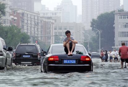 Un hombre sentado sobre un coche atrapado por las lluvias, en una calle de la ciudad de Tianjin, China, el miércoles 20 de julio. 