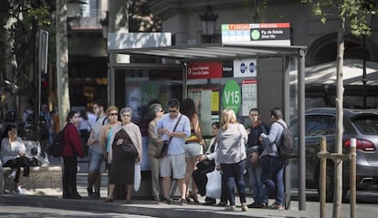 Ciudadanos y turistas esperan en una de las paradas del paseo de Gràcia que van al Park Güell.