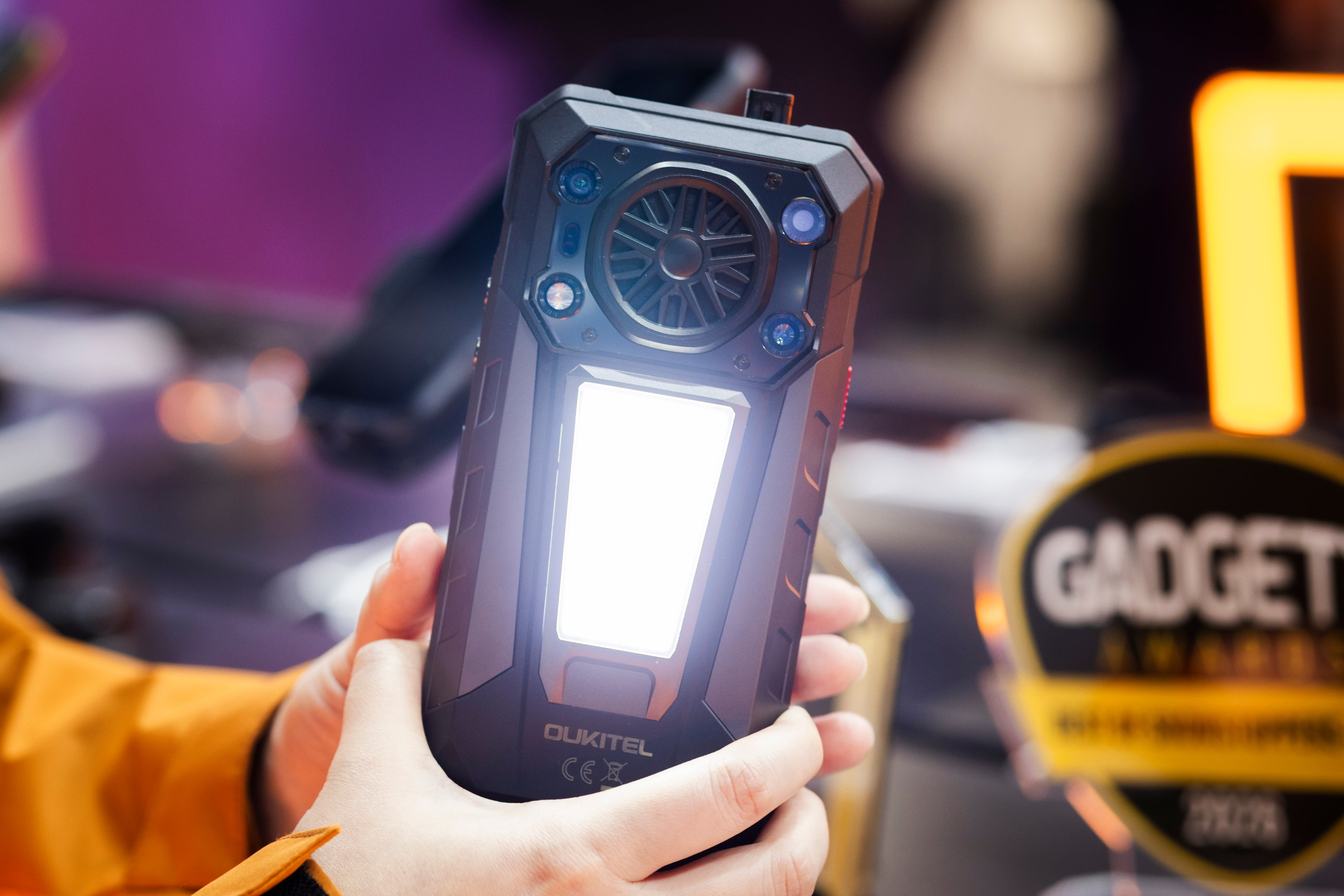 Móvil que tiene linterna grande, batería externa, y mechero,  en el stand de Oukitel.