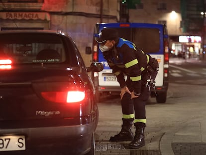 Un policía local se acerca a hablar con ciudadanos que están en un coche en Salamanca, la noche en la que la ciudad vivió el sábado su primer toque de queda dictado por la Junta de Castilla y León para toda la región.