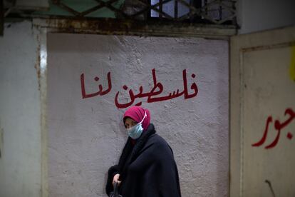 Una mujer camina entre las callejuelas del campo de refugiados de Chatila. A su espalda, se puede leer la frase "Palestina nuestra", escrita en árabe.