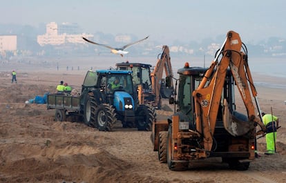 Operarios de limpieza ayudados de maquinaria recogen las toneladas de residuos abandonados en la playa América de Nigrán (Vigo) tras las celebraciones de las hogueras de la noche de San Juan con el fin de dejar la playa en condiciones para su uso diurno.