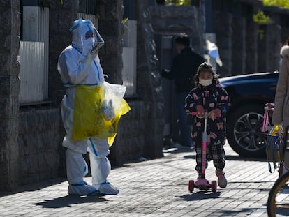 Una niña con mascarilla pasa junto a un trabajador que recoge muestra de control de la covid, este jueves en Pekín.