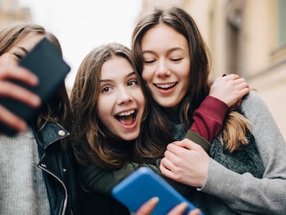 Girl taking selfie with female friends through mobile phone in city