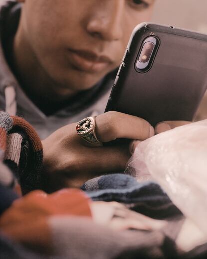 San Pedro Sacatepéquez, San Marcos; 2019.
Un adolescente, absorto en las redes sociales en su teléfono,
vende trapos de limpieza en el mercado de la ciudad. Esta imagen habla dos temas clave en las tierras altas: el papel fundamental de los 'smartphones' y la tecnología en desarrollo, fomentando conexiones con el mundo; y la creciente influencia de la 'narcocultura'. En su dedo, un gallo canta en un anillo, un símbolo sutil pero potente del entrelazamiento de la tradición y la modernidad. Cada día que pasa, los símbolos del narco se vuelven cada vez más normalizados, reflejando su creciente prominencia en la cultura pop y destacando las dinámicas sociales complejas que configuran la vida en el Altiplano Central.