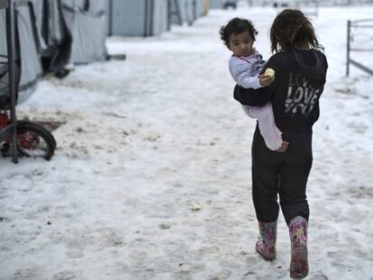 Una ni&ntilde;a siria camina con su hermana en brazos en el campo de Ritsona, en Grecia.