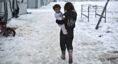 Una ni&ntilde;a siria camina con su hermana en brazos en el campo de Ritsona, en Grecia.