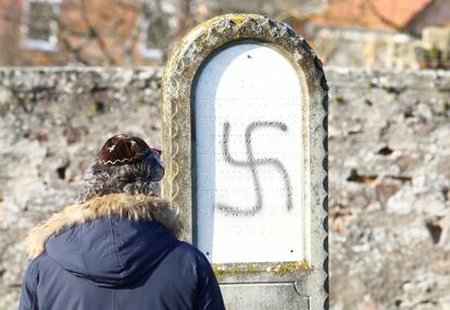 En la imagen un hombre mira una tumba profanada con una esvástica.