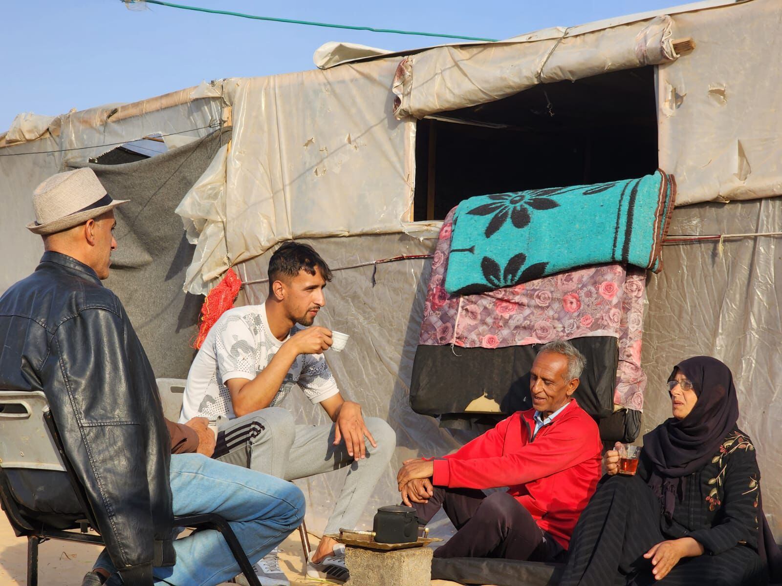 Abed Raboo Kilany, en cuclillas (centro) conversa con miembros de su familia y con su entrenador, Amjed Tantish (izquierda) en un campo de desplazados en Rafah, en el sur de la Franja de Gaza, en mayo de 2024