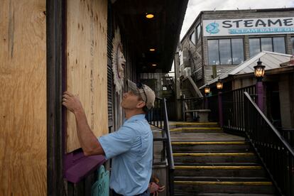 Un hombre protege con madera las ventanas de una tienda antes de la llegada del huracán en Cedar Key, Florida.