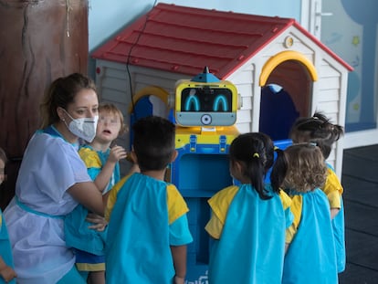 Una educadora muestra a los niños un robot que toma la temperatura en una escuela infantil, esta mañana en Madrid