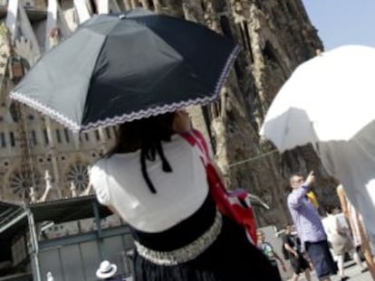 Unas turistas se protegen del intenso calor con paraguas ante la basílica de la Sagrada Familia de Barcelona.