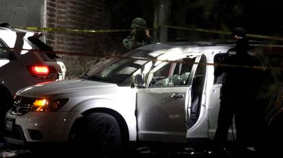 Soldados y policías observan un coche tiroteado.