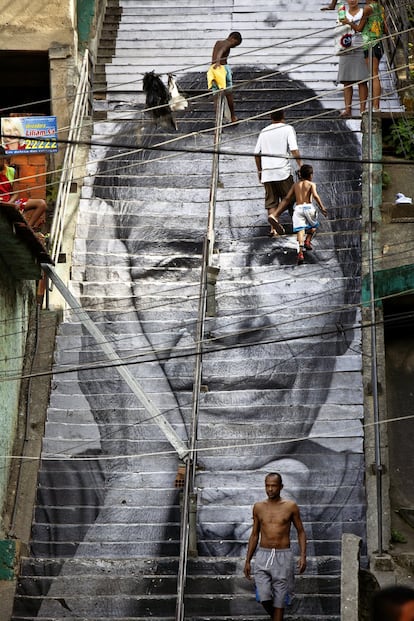 Uma primeira intervenção, interrompida temporariamente por um tiroteio, mudou tudo. JR e sua equipe cobriram a enorme escada que atravessa a parte alta da favela, território de disputa entre traficantes e policiais, com a imagem da avó de um dos meninos assassinados. Os moradores a reconheceram e entenderam o poder do papel e da cola. Eles, na verdade, queriam falar e ninguém parecia dar atenção. Até os traficantes permitiram que o francês passasse 25 dias cobrindo suas fachadas de tijolo com os rostos doloridos das mães, amigas e avós daqueles meninos — mulheres anônimas que só queriam um bairro melhor.