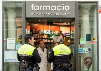 Dos agentes de la Policía Local de Sevilla hablan con un farmacéutico en la puerta de su establecimiento en la capital andaluza.