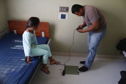 Selena observa a su padre Luis mientras revisa la batería de un localizador GPS, acogidos en un alberge poco después de haber sido reunificados.