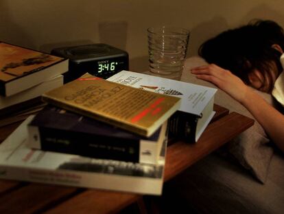 Una mujer durmiendo, con varios libros en la mesilla, junto al reloj despertador.