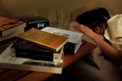 Una mujer durmiendo, con varios libros en la mesilla, junto al reloj despertador.