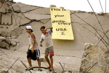 Dos niños caminan entre ruinas en la ciudad de Tiro (sur de Líbano), donde pueden verse carteles dirigidos a EE UU que rezan: "Esta es tu democracia".