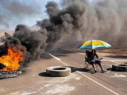 Chile. Un manifestante se sienta bajo un paraguas mientras bloquea una ruta de acceso a Iquique durante un paro regional convocado por diferentes organizaciones contra la inmigración ilegal. La ciudad de Iquique, en el norte de Chile y cerca de la frontera con Bolivia vivió este lunes una segunda jornada de agitación con bloqueos en sus vías de ingreso y el cierre de su aeropuerto, en protesta por el aumento de la delincuencia que algunos asocian con la inmigración ilegal.