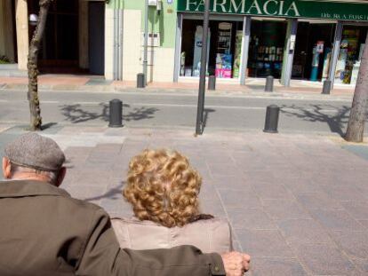 Una pareja de pensionistas ante una farmacia.
