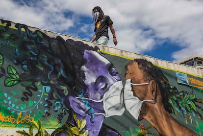 Homem com máscara passa por graffiti de Marcos Costa, o Spray Cabuloso, na entrada da favela Solar de Unhão em Salvador, Bahia, em 15 de abril.