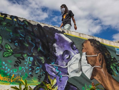 Homem com máscara passa por graffiti de Marcos Costa, o Spray Cabuloso, na entrada da favela Solar de Unhão em Salvador, Bahia, em 15 de abril.