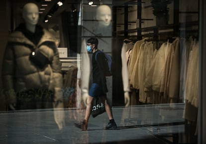 Reflejo en el escaparate de una tienda de un joven mientras camina con mascarilla por Portal de l'Àngel, en Barcelona.