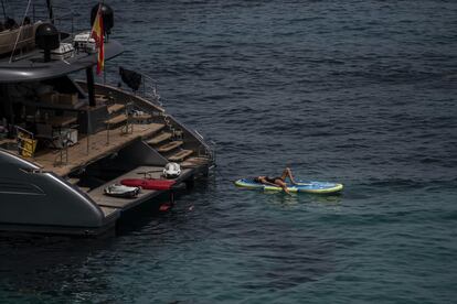 Una mujer toma el sol en una tabla junto a un barco, en la cala Comte.