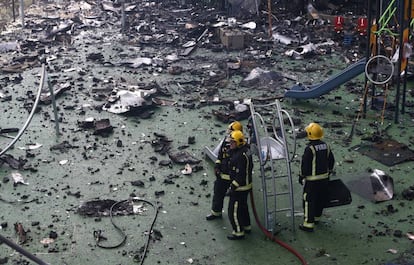 Bomberos trabajan en un patio con columpios infantiles cerca del edificio siniestrado en Kensington, Londres.