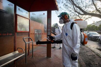 Un operario desinfecta una parada de autobús en el barrio de La Garena, este viernes, en Alcalá de Henares.