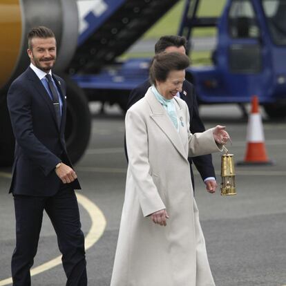 La princesa Ana de Inglaterra sostiene la linterna con la llama olímpica junto al futbolista británico David Beckham