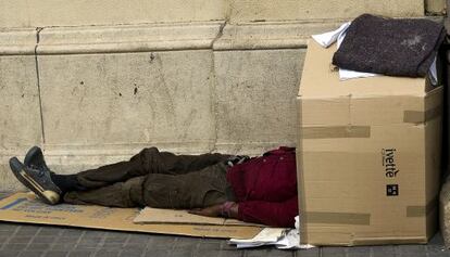 Una persona duerme bajo cartones en plena plaza de Catalunya.