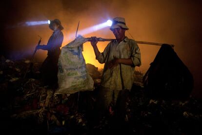 Una pareja busca entre la basura con la iluminación de las hogueras y la luz de sus linternas.