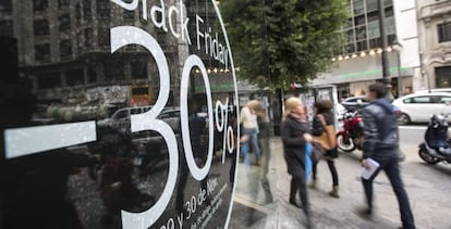 Varias personas pasan ante un comercio de una c&eacute;ntrica calle de Valencia que anuncia descuentos del 30% en el llamado &#039;Black Friday&#039; (Viernes Negro). 