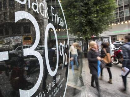 Varias personas pasan ante un comercio de una c&eacute;ntrica calle de Valencia que anuncia descuentos del 30% en el llamado &#039;Black Friday&#039; (Viernes Negro). 