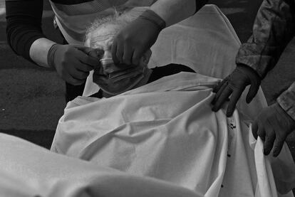 Alberto ayuda a una anciana a colocarse una mascarilla antes de su traslado al Hospital Universitario Central de Asturias desde la residencia de ancianos Las hermanitas desamparadas, en Pola de Siero.
