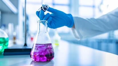 Close up of unrecognizable chemist pouring purple liquid into a beaker at laboratory. Focus is on flask. Copy space.
