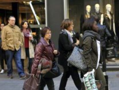 Varias personas transitan una c&eacute;ntrica calle de Barcelona tras realizar algunas compras, durante la jornada del domingo del Puente de la Constituci&oacute;n.