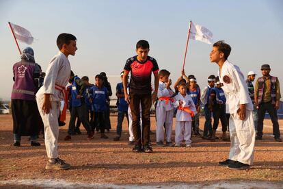 Bajo la mirada del público, dos chicos con atuendos de karateka y cinturones naranjas, se miran y saltan gritando, con un pie delante del otro y lanzando puñetazos en el aire.