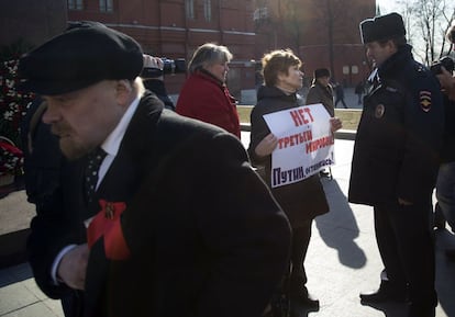 Um policial conversa com uma mulher que segura um cartaz que diz "Não queremos a Terceira Guerra, Putin pare!" próximo à Praça Vermelha em Moscou, na Rússia. No primeiro plano, um homem passeia vestido com roupa similar à do fundador da URSS Vladimir Lenin.