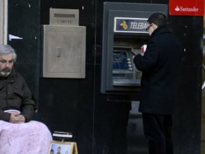 Um homem pede esmolas na porta de um caixa automático em Madri.
