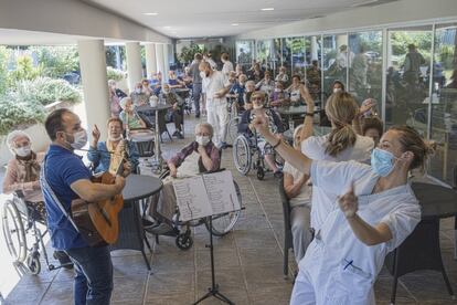 Juanjo Pérez toca la guitarra para los residentes del centro de mayores Mas Camarena de Bétera, en Valencia, junto a la terapeuta ocupacional Lucía Antón y otros trabajadores de la institución que bailan.