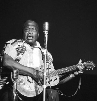  He aquí un hombre, Bukka White (Misisipi, 1906-Tennessee, 1977), que en dos ocasiones estuvo en un oscuro agujero muy distanciado de la música y en ambas fue rescatado por entusiastas arqueólogos musicales. En la primera le vemos (condenado por disparar a una persona) en una sombría celda de la cárcel de Parchman Farm, la durísima penitenciaría de Misisipi. Hablamos de ser un presidiario negro en los años cuarenta en la racista Estados Unidos. Los reclusos trabajaban en unas condiciones insoportables desde que se ponía el sol y hasta que llegaba la noche. Hasta allí llegó el musicólogo Alan Lomax (impagable su labor) para grabarle unas canciones. Cuando salió de la cárcel, White, grande del blues del delta, registró una colección de piezas estremecedoras sobre su experiencia carcelaria. Pero volvió a desaparecer. Fue llamado a filas para participar en la II Guerra Mundial y cuando regresó a Memphis acabó trabajando de chatarrero. Eras los sesenta y sus canciones eran reivindicadas por figuras como Bob Dylan o los Rolling Stones. Dos aficionados al folk fueron a su encuentro y le contaron la pasión que por su música tenían músicos blancos. Le convencieron para que volviera a cantar. Vivió unos años de giras con cierto éxito e incluso ayudó a componer a su primo, B.B.King. Falleció en 1977, con 71 años, víctima de un cáncer. En la imagen, Bukka White en el Folk Blues Festival en 1967.