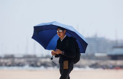 Un hombre caminaba este miércoles por la playa de la Malvarrosa, en Valencia, con un paraguas para protegerse del sol.