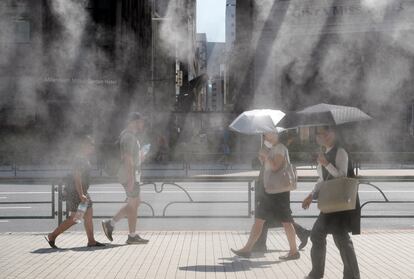 Varias personas caminan por una calle con agua vaporizada en la ciudad de Tokio (Japón), el 11 de julio. 
